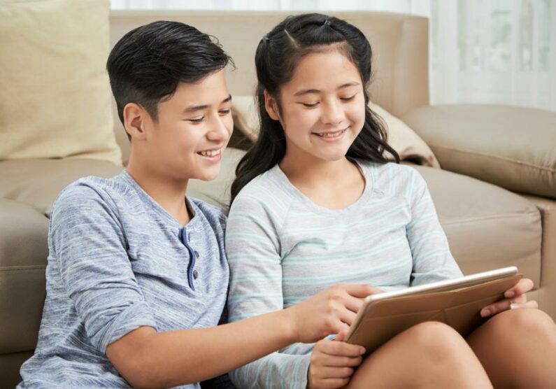 Smiling,Mixed-race,Brother,And,Sister,Reading,Something,On,Tablet,Computer